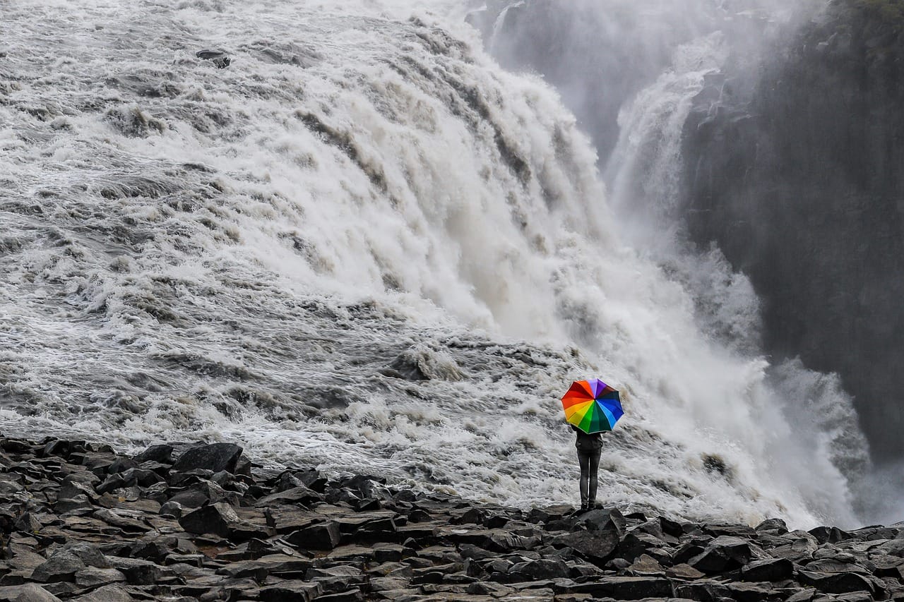 Person with a colorful umbrella standing next to a waterfall