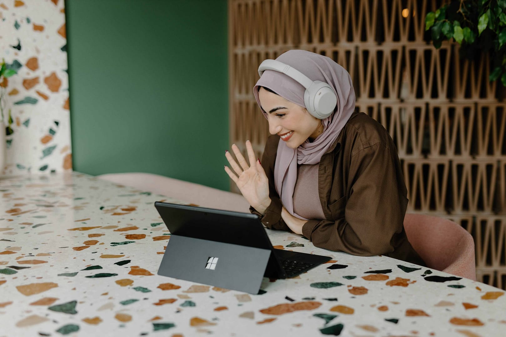 Woman with headphones waving hello at a laptop