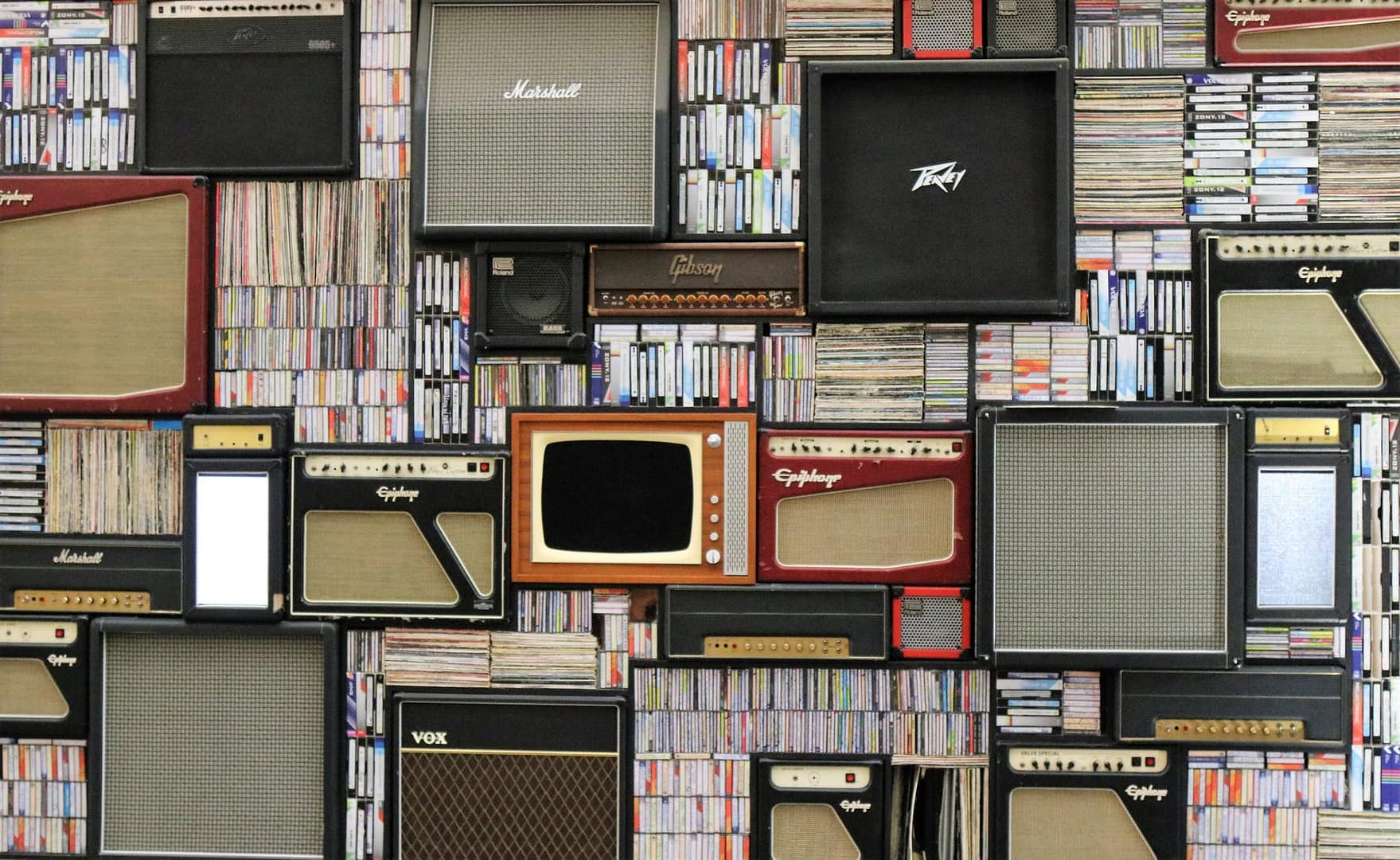 assorted guitar amplifiers stacked among tapes and records