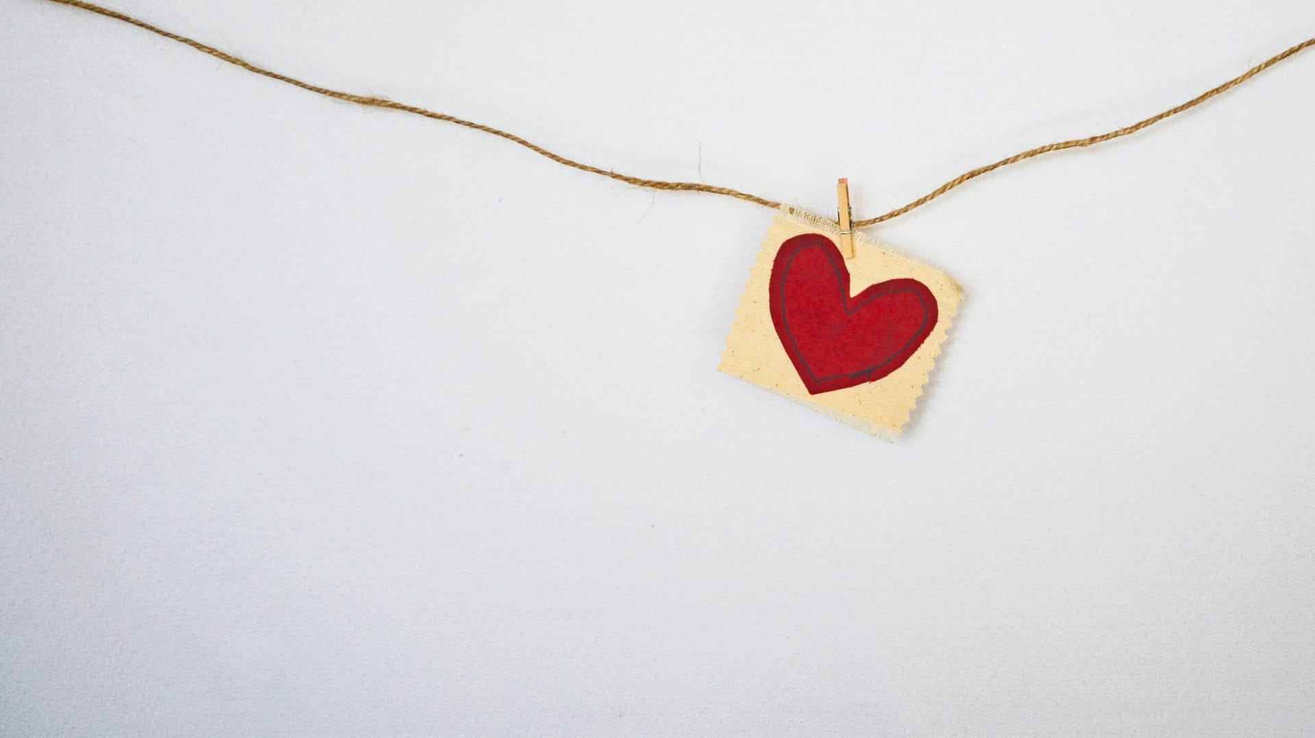 A small yellow square with a heart on it is pinned to a cord strung across a white background. Evokes a feeling of love