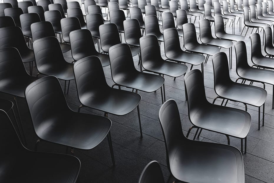 Rows of empty black chairs arranged in a grid pattern, suggesting a formal setting like a classroom or lecture hall.