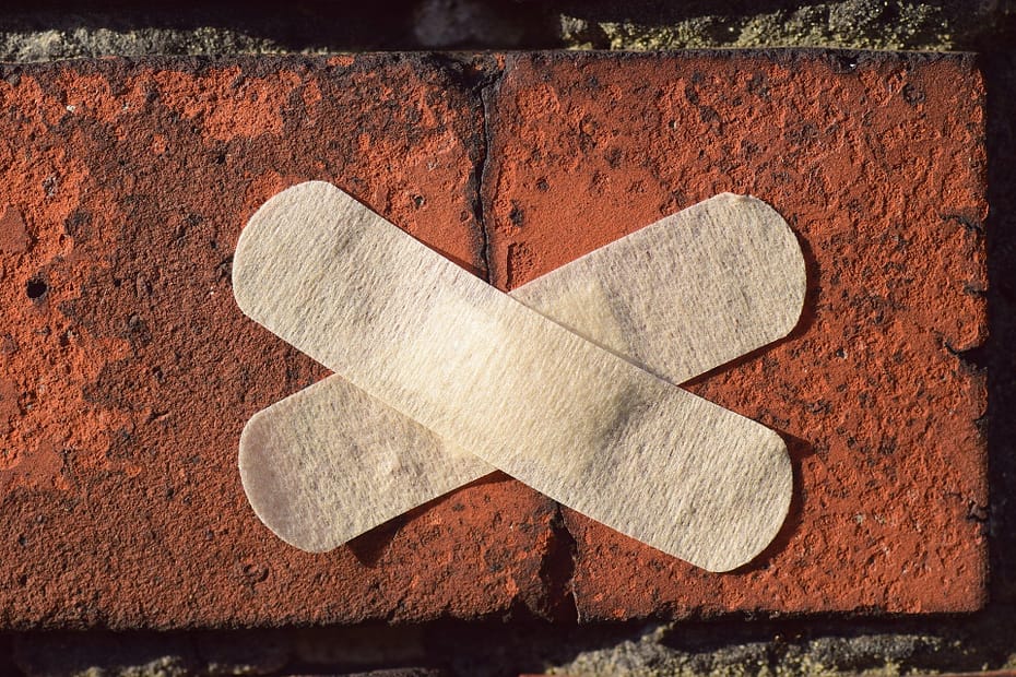 two baind-aids crossed to make an x over a crack in a brick wall.