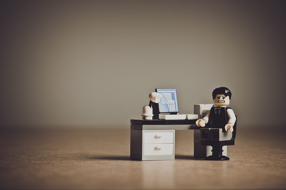 Lego man sits at a desk with a lego computer, he has a grimacing look on his face