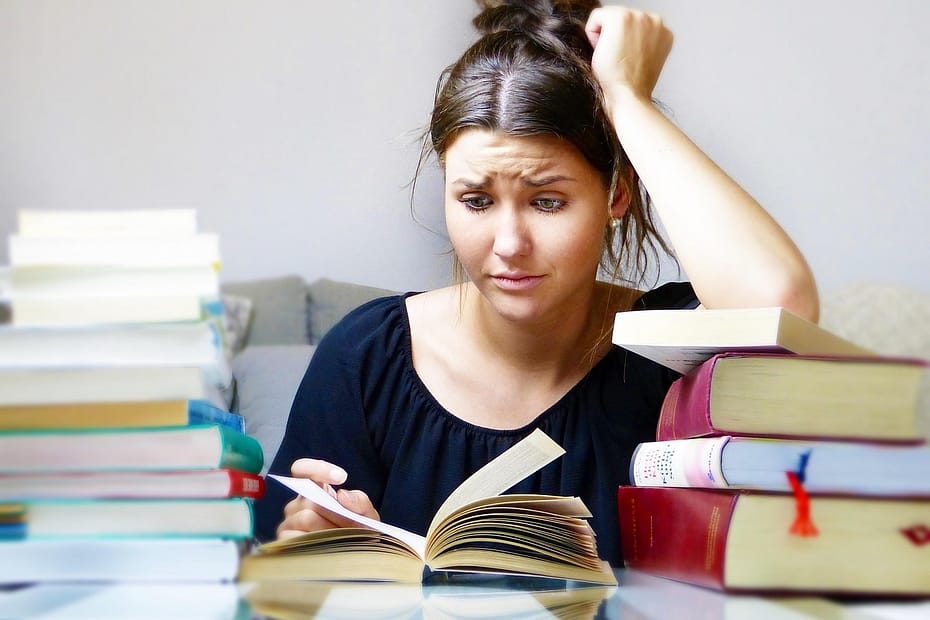 Woman looking stressed while studying with large stacks of books.