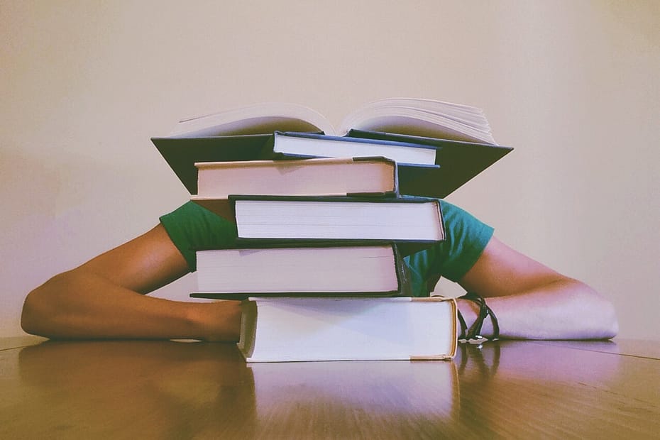 Person slumped at a table behind a tall stack of books.