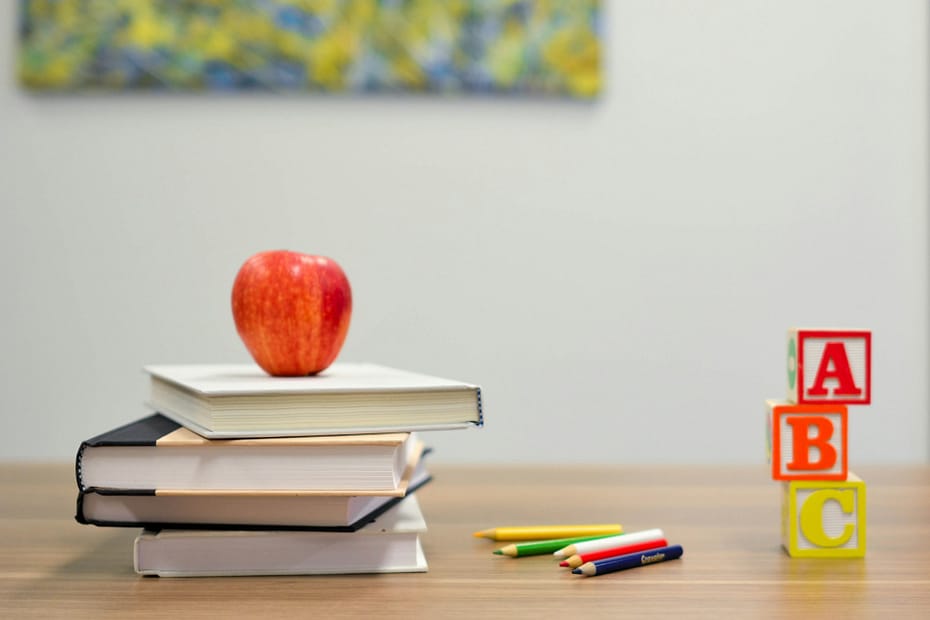 apple placed on top of some books next to coloring pencils and A, B, C letter blocks